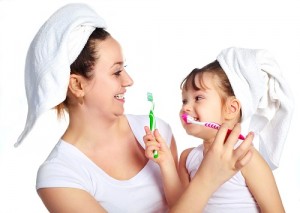 young beautiful mother and her little daughter brushing teeth and laughing