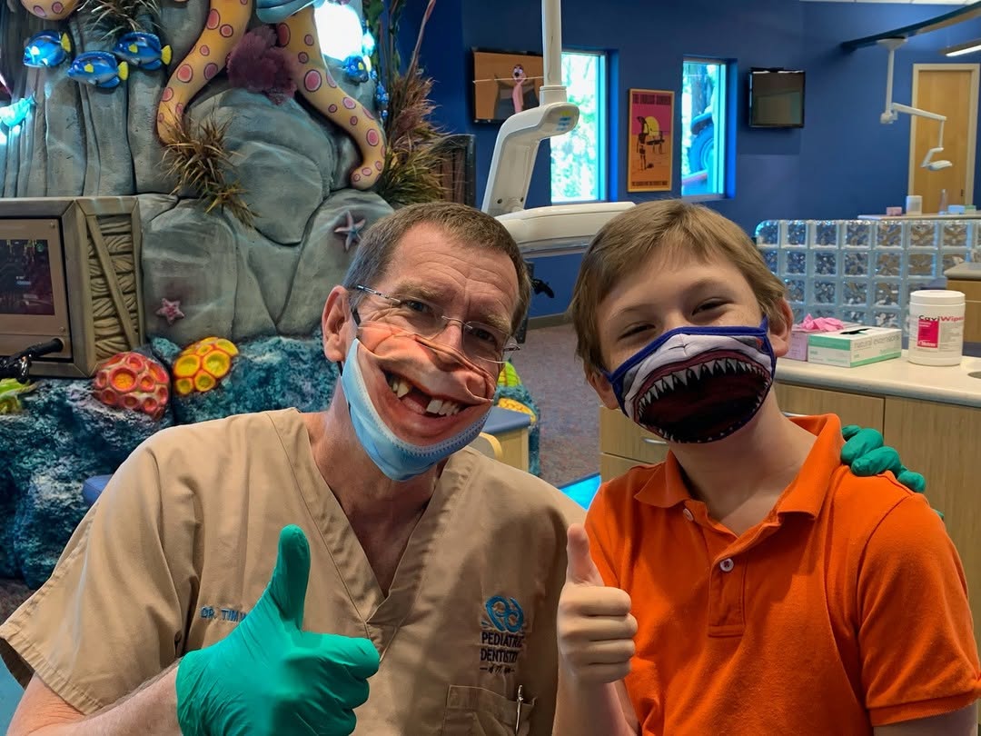 Dr. Verwest and a young patient wearing funny teeth masks and giving thumbs up